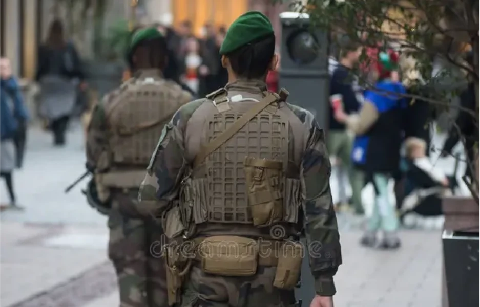 Deux soldats en uniformes de camouflage et bérets verts marchent dans une rue animée de la ville, transmettant un sentiment de sécurité et de vigilance.