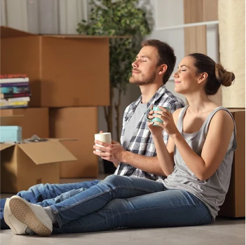 Un couple marche bras dessus bras dessous sur une plage ensoleillée, éclairée par le coucher de soleil doré. Ils portent des chaussures, évoquant chaleur, détente et complicité.
