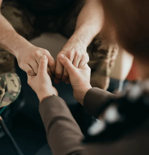 Une personne en uniforme militaire est assise, les mains tenues par une autre personne de manière encourageante, transmettant réconfort et empathie dans un cadre de conseil.
