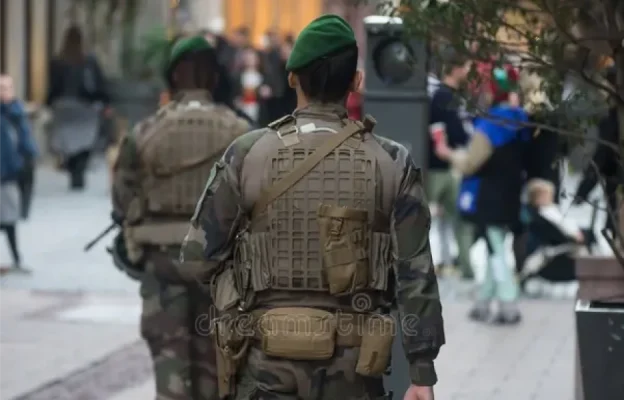 Deux soldats en uniformes de camouflage et bérets verts marchent dans une rue animée de la ville, transmettant un sentiment de sécurité et de vigilance.