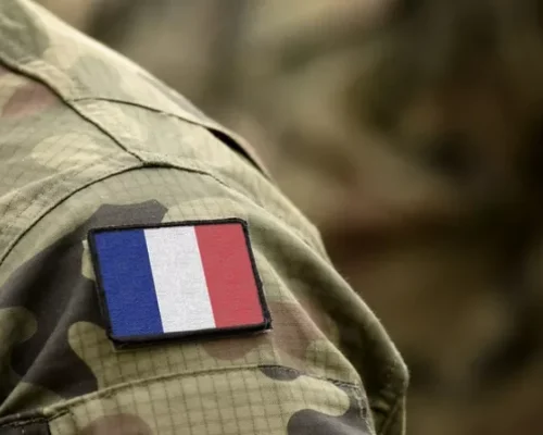 Un écusson du drapeau français sur la manche d'un uniforme militaire camouflage. Le ton est sérieux et patriotique, soulignant l'unité et l'identité.